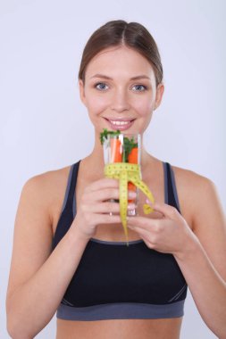 Elinde bir bardak dolusu taze meyve salatası ve bardağın etrafında mezura tutan bir kadın..