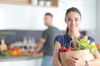 Mutfakta genç bir çift, alışveriş torbası taşıyan bir kadın.
