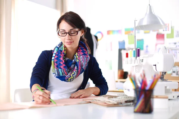 Güzel moda tasarımcısı stüdyoda masada oturuyor. .