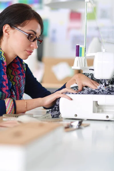 Junge Frau näht, während sie am Arbeitsplatz sitzt . — Stockfoto