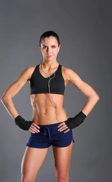Muscular young woman posing in sportswear against black background. — Stock Photo, Image