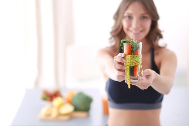 Elinde bir bardak dolusu taze meyve salatası ve bardağın etrafında mezura tutan bir kadın..