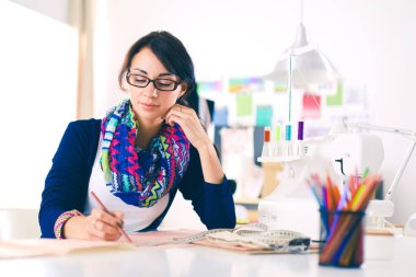 Güzel moda tasarımcısı stüdyoda masada oturuyor. .