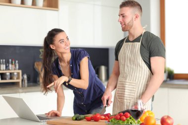 Sebze doğrayan genç bir adam ve mutfakta dizüstü bilgisayarı olan bir kadın.
