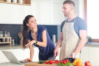 Sebze doğrayan genç bir adam ve mutfakta dizüstü bilgisayarı olan bir kadın.