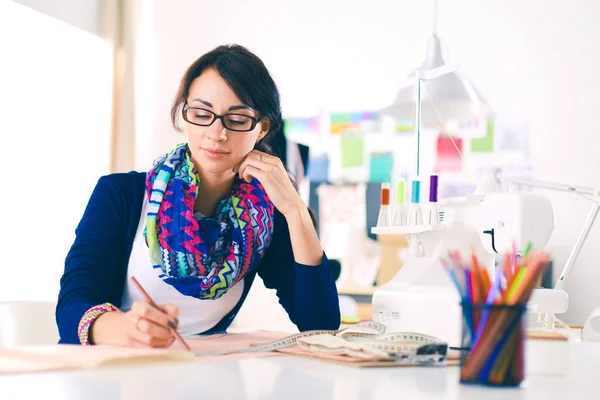 Güzel moda tasarımcısı stüdyoda masada oturuyor. .