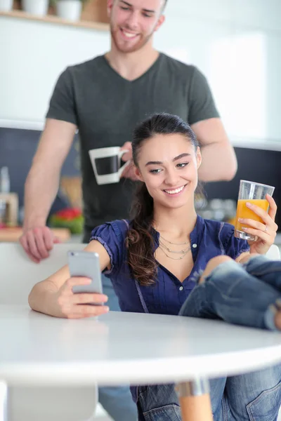 Pareja feliz usando smartphone sentado en la cocina — Foto de Stock