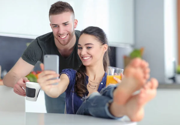 Pareja feliz usando smartphone sentado en la cocina — Foto de Stock