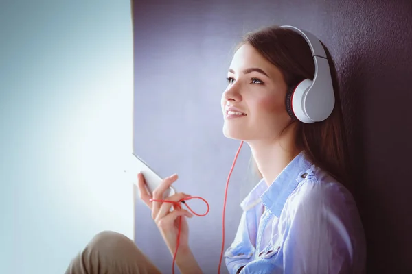 Smiling girl with headphones sitting on the floor near wall — Stock Photo, Image