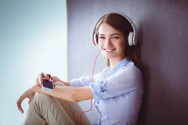 Chica sonriente con auriculares sentados en el suelo cerca de la pared —  Fotos de Stock