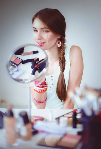 Joven hermosa mujer haciendo maquillaje cerca del espejo, sentado en el escritorio — Foto de Stock