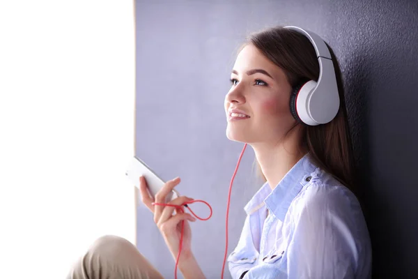 Ragazza sorridente con le cuffie seduto sul pavimento vicino al muro — Foto Stock