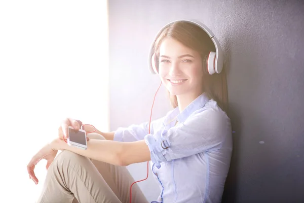 Ragazza sorridente con le cuffie seduto sul pavimento vicino al muro — Foto Stock