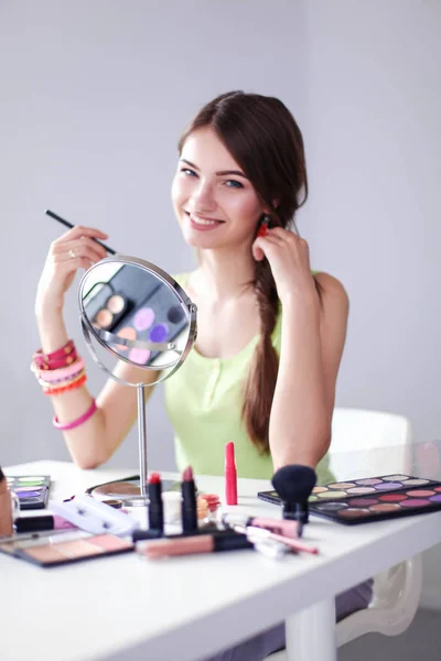 Молода красива жінка робить макіяж біля дзеркала, сидить за столом — стокове фото