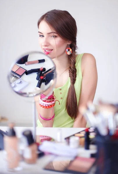 Joven hermosa mujer haciendo maquillaje cerca del espejo, sentado en el escritorio — Foto de Stock