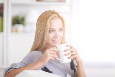 Genç bayan kanepede dinleniyor ve ışık odasında çay içiyor.