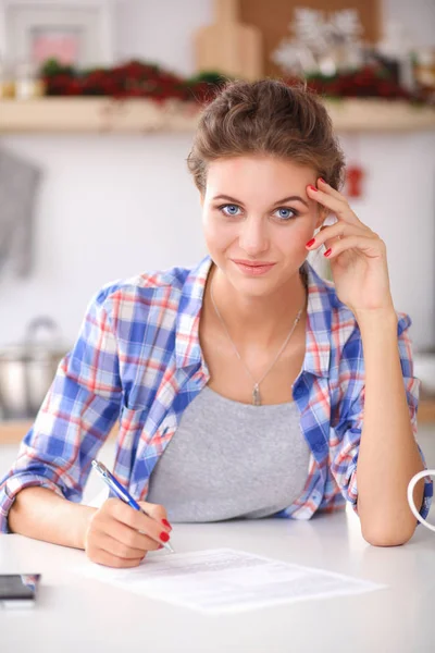 Feliz hermosa mujer de pie en su cocina escribiendo en un cuaderno en casa — Foto de Stock