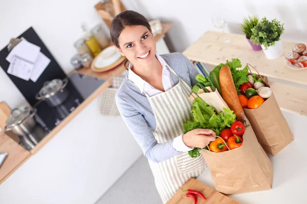 Ung kvinna som håller i matkassen med grönsaker. Stående i köket — Stockfoto