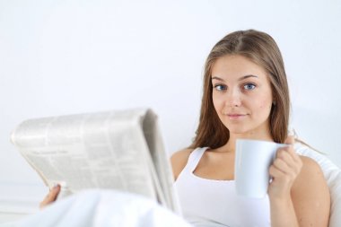 Genç ve güzel bir kadın yatakta gazete okuyan ve bir fincan çay keyfi.