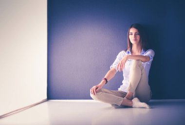 Genç bir kadın yerde, kara duvarın yanında oturuyor.