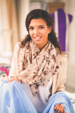 Gülümseyen kadın moda tasarımcısı ofis masasında oturuyor.