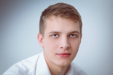 Gri arka plan üzerinde oturan gülümseyen genç adam portresi