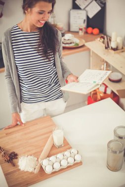Mutlu genç kadın Noel süslemeli mutfakta saat gösteriyor.