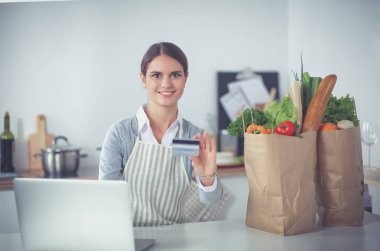 Mutfakta bilgisayar ve kredi kartı kullanan gülümseyen bir kadın.