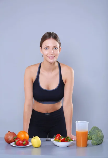 Mujer joven y hermosa de pie cerca del escritorio con verduras. — Foto de Stock