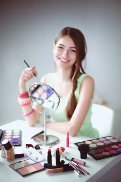 Joven hermosa mujer haciendo maquillaje cerca del espejo, sentado en el escritorio —  Fotos de Stock