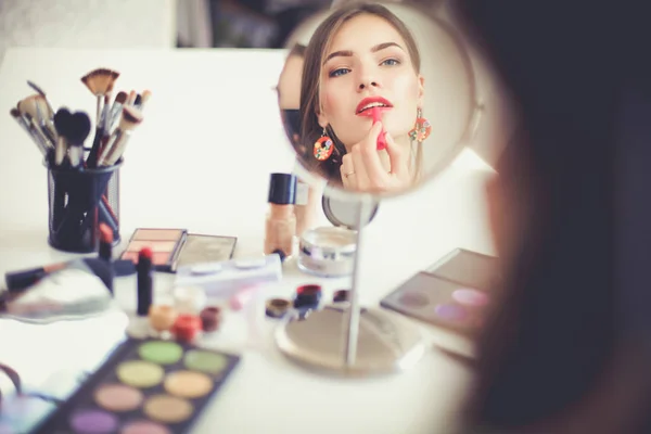 Jovem bela mulher fazendo maquiagem perto do espelho, sentado na mesa — Fotografia de Stock