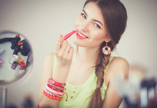 Joven hermosa mujer haciendo maquillaje cerca del espejo, sentado en el escritorio —  Fotos de Stock