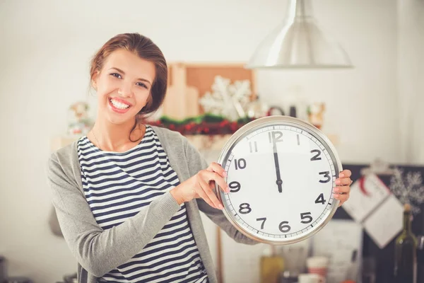Happy young woman showing clock in christmas decorated kitchen — Stock Photo, Image