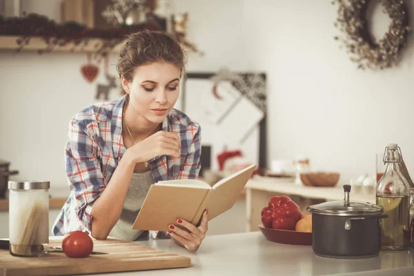 Mujer joven leyendo libro de cocina en la cocina, buscando receta — Foto de Stock