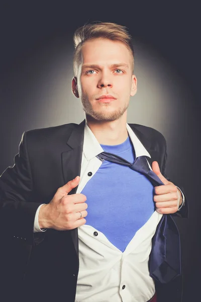 Młody biznesmen działający jak super hero i łzawienie koszulę, na białym tle na szarym tle — Zdjęcie stockowe