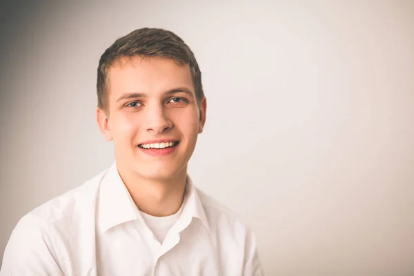 Retrato de un joven sonriendo sentado sobre un fondo gris — Foto de Stock