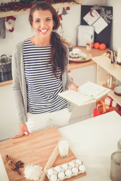 Glückliche junge Frau zeigt Uhr in weihnachtlich dekorierter Küche — Stockfoto