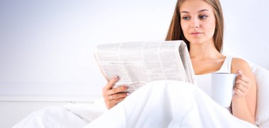 Genç ve güzel bir kadın yatakta gazete okuyan ve bir fincan çay keyfi.