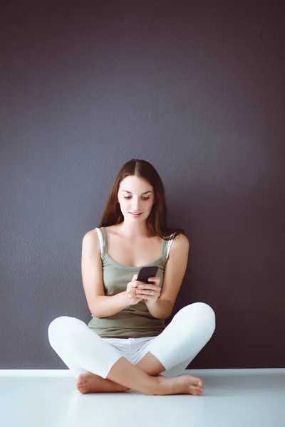 Attraente ragazza caucasica seduta sul pavimento con tazza e tablet vicino alla parete — Foto Stock