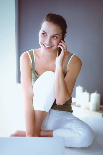 Lächelnde schöne Brünette, die auf dem Boden sitzt und ihr Handy im Wohnzimmer benutzt — Stockfoto