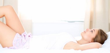 Güzel genç bir kadın, rahat ve mutlu bir şekilde yatakta uzanıyor.