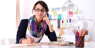 Güzel moda tasarımcısı stüdyoda masada oturuyor. .