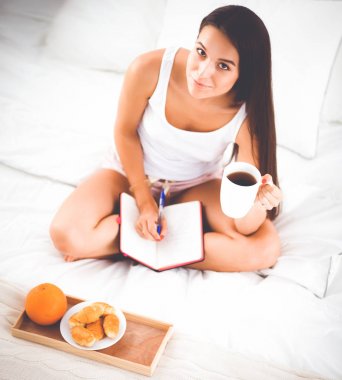 Yatakta oturmuş ve bir defterini yazma genç güzel kadın