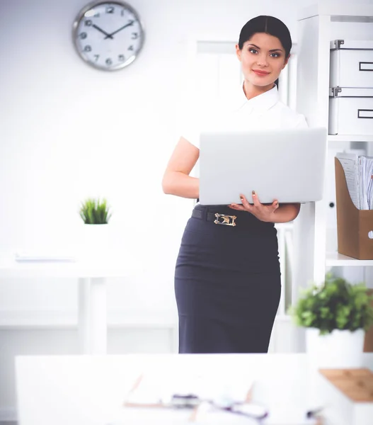 Attractive businesswoman standing in office with laptop — Stock Photo, Image