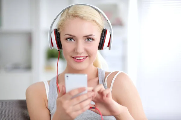 Jeune belle femme à la maison assise sur un canapé et écoutant de la musique — Photo