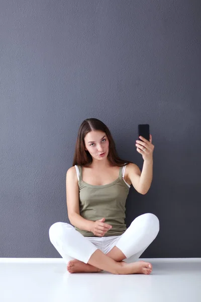 Atractiva chica caucásica sentada en el suelo con taza y tableta cerca de la pared — Foto de Stock