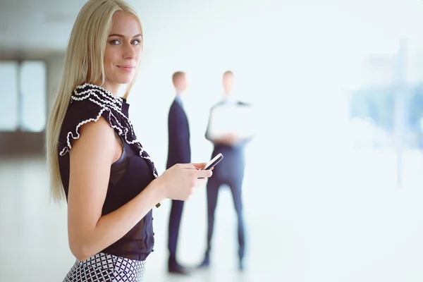 Mulher de negócios bonita usando telefone celular, de pé no escritório . — Fotografia de Stock