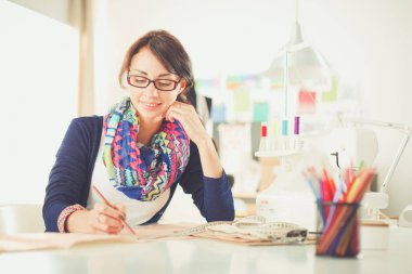 Güzel moda tasarımcısı stüdyoda masada oturuyor. .