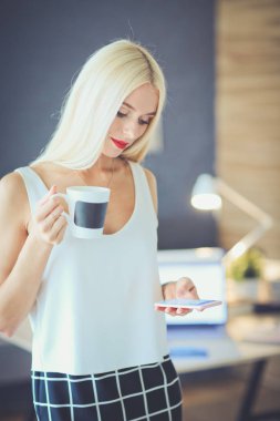 Genç iş kadını elinde fincanla masada oturuyor.