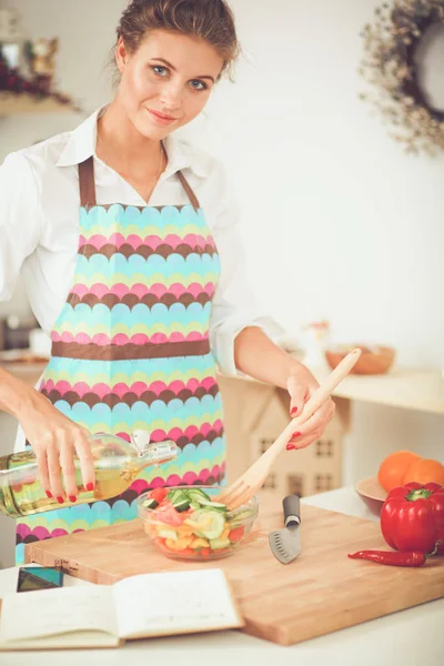 Улыбающаяся молодая женщина готовит салат на кухне . — стоковое фото